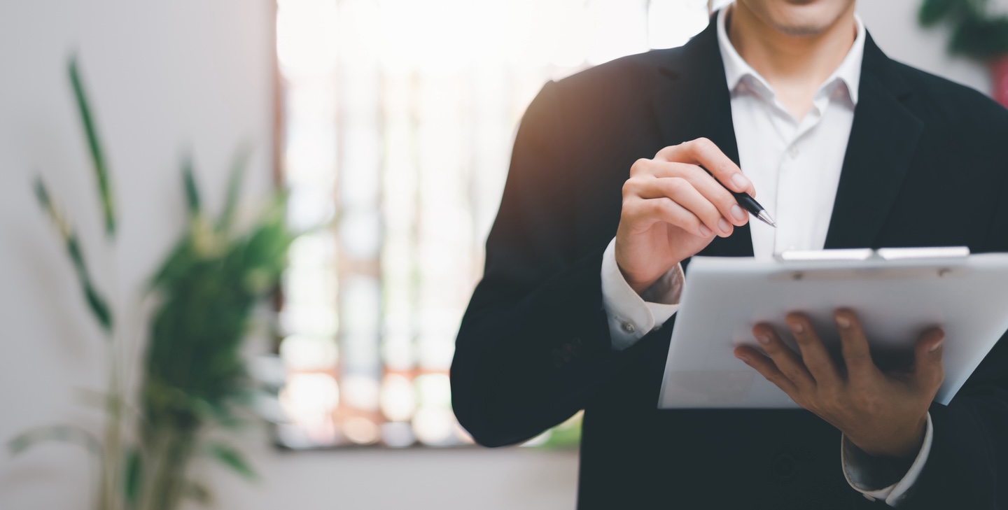 Business person pointing at clipboard with pen.