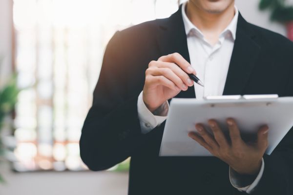 Business person pointing at clipboard with pen.